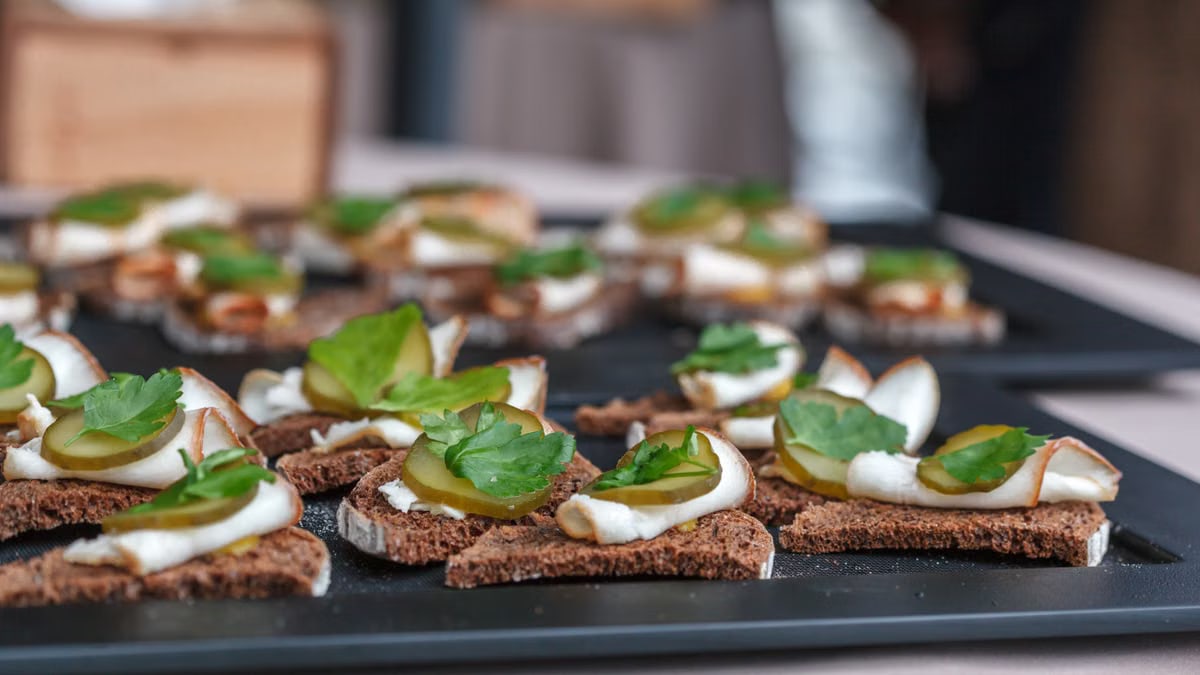 Delicious canapés with ham, pickles, and parsley on brown bread for a refreshing snack.